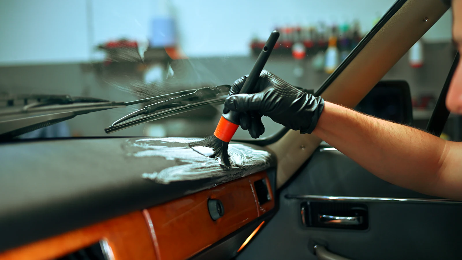 Hand mit Handschuh reinigt das Armaturenbrett eines Autos mit einer Bürste
