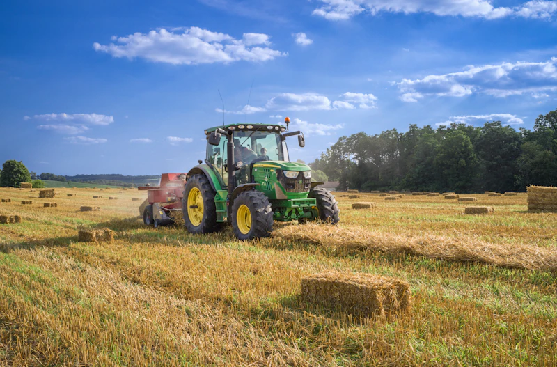 Grüner Traktor auf einem abgeernteten Feld unter blauem Himmel
